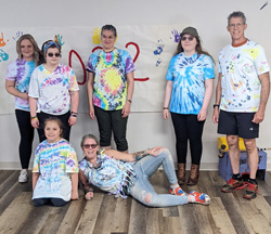 Staff and students wearing their tie-dye t-shirts, standing against a wall