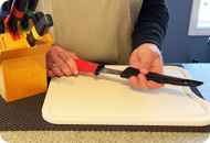 A knife is being slid into a protective sleve, other knives can be seen sitting in a knife holder.