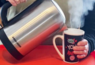 Hot water being poured from a kettle to a cup, steam can be seen rising from the cup