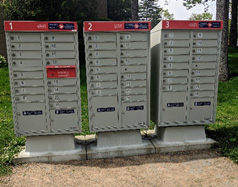 Three grey community mailboxes, each with sixteen individual boxes. There are two boxes for larger parcels and packages on the bottom of each community mailbox.