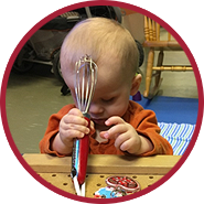 Preschooler exploring different objects, holding a kitchen utensil