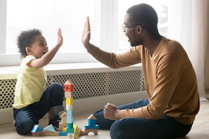 a child and father about to high-five, building blocks piled into a tower on the floor