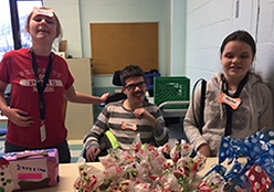 Three students stand behind a counter selling their packaged dog treats. A donation box sits to the left